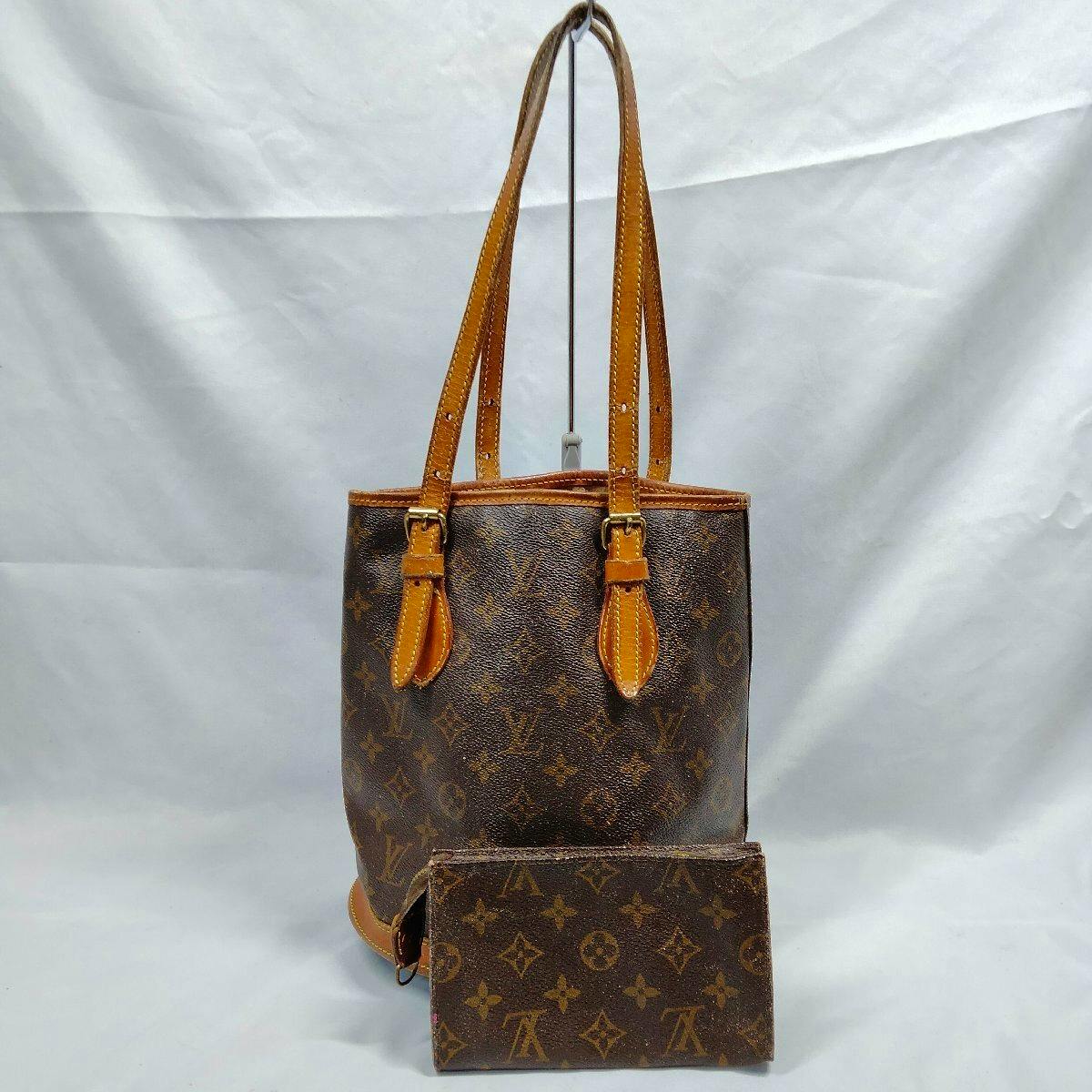 Front view of a Louis Vuitton monogram Bucket PM bag with leather shoulder straps and a matching monogram pouch placed in front.