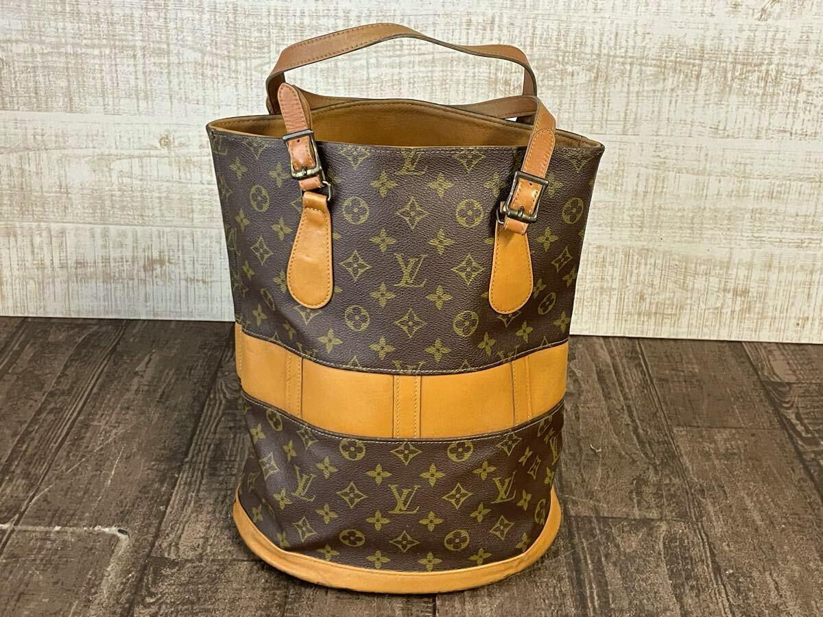 Front view of a Louis Vuitton monogram bucket tote bag with tan cow leather trim and handles.