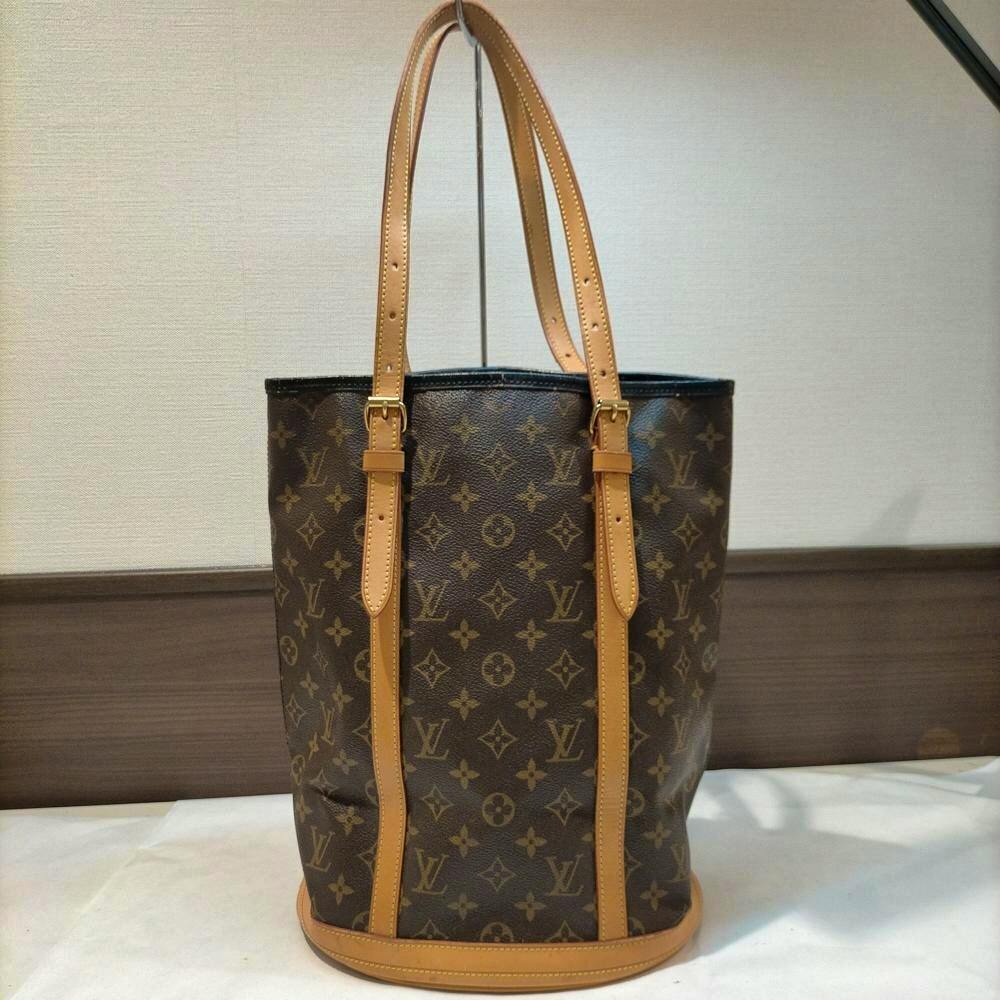 Brown Louis Vuitton monogram bucket tote bag with tan leather straps displayed upright.
