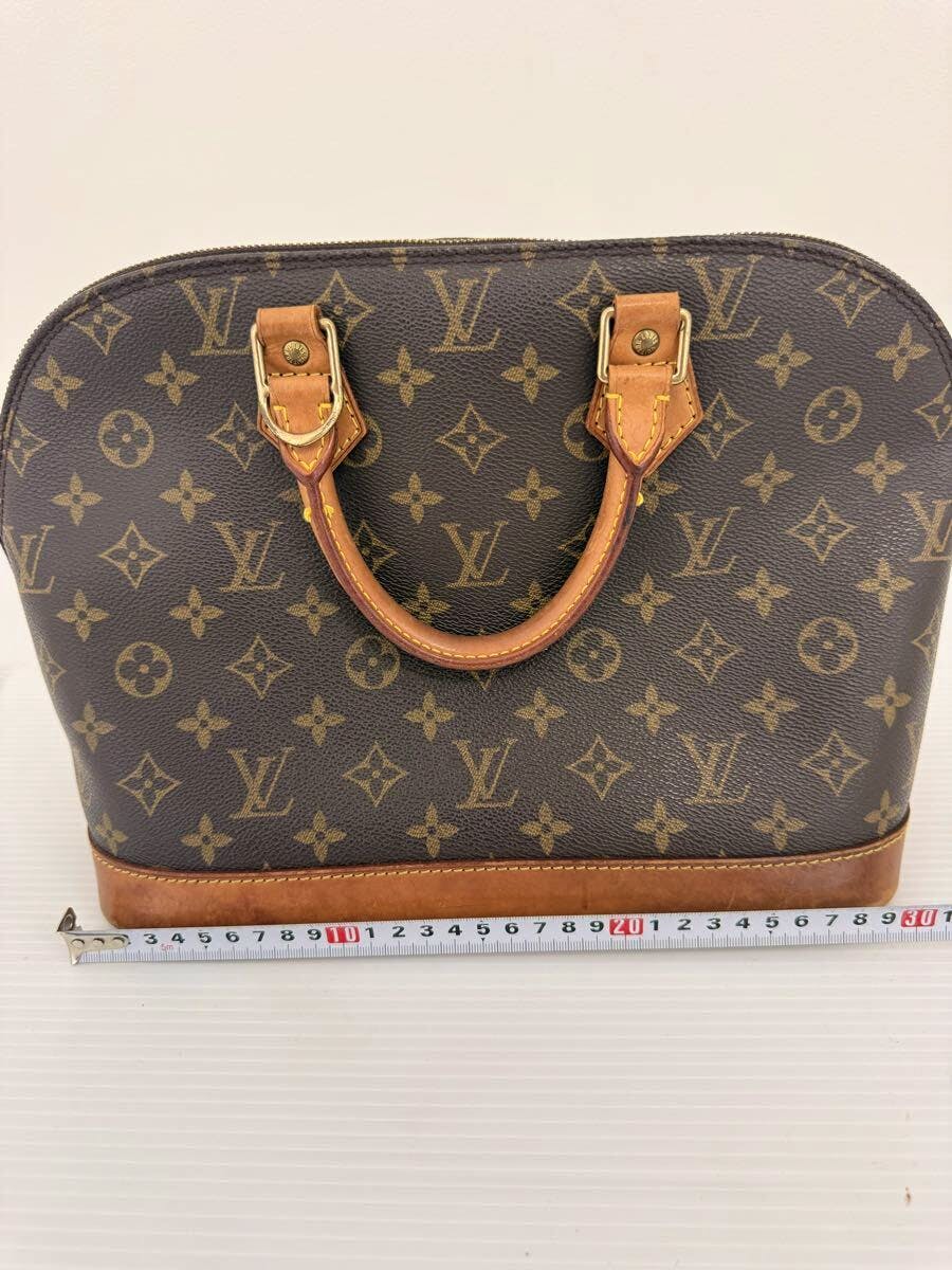 Front view of a Louis Vuitton monogram canvas bag showing its top handles and monogram pattern with a measuring tape at the base.