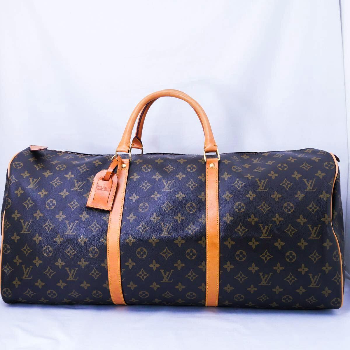 Monogram canvas Louis Vuitton travel duffel bag with tan leather handles and straps on a white background.