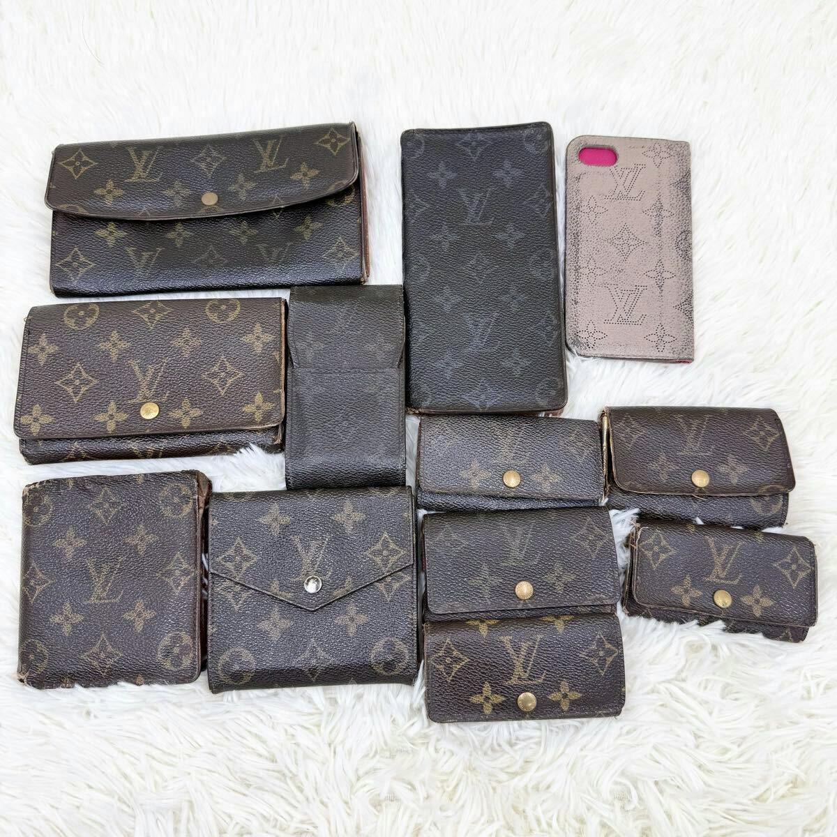 Multiple Louis Vuitton monogram wallets and small leather goods arranged on a white fur background.