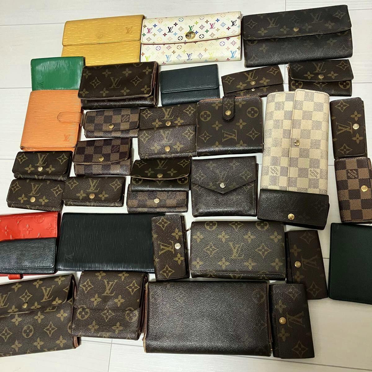 An assortment of Louis Vuitton wallets and small leather goods in monogram, Damier, and Epi patterns arranged on a floor.
