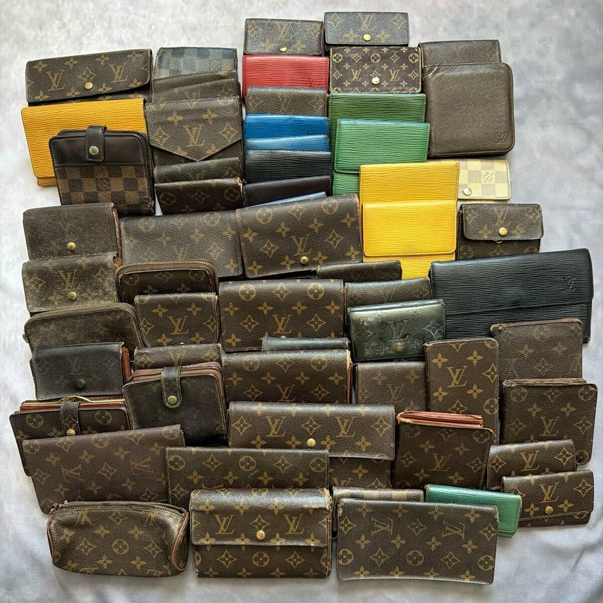 Top-down photo of many Louis Vuitton wallets and small leather goods in monogram, Damier, and Epi styles arranged on a light gray surface.