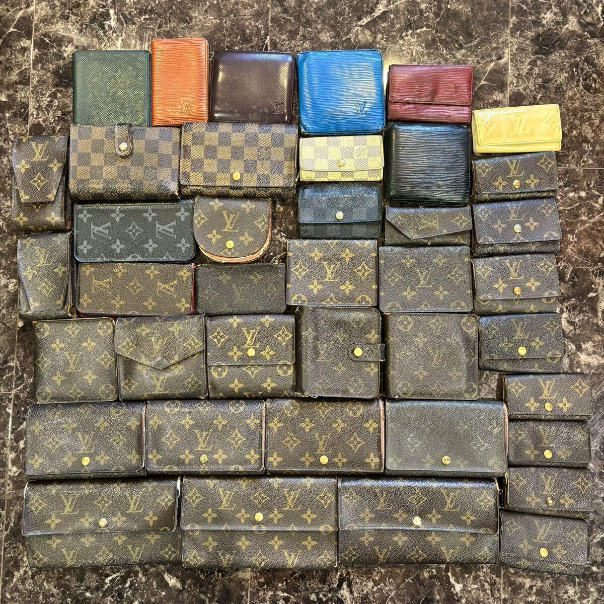 Multiple Louis Vuitton wallets and coin cases in monogram, Damier, and Epi patterns arranged on a marble surface.