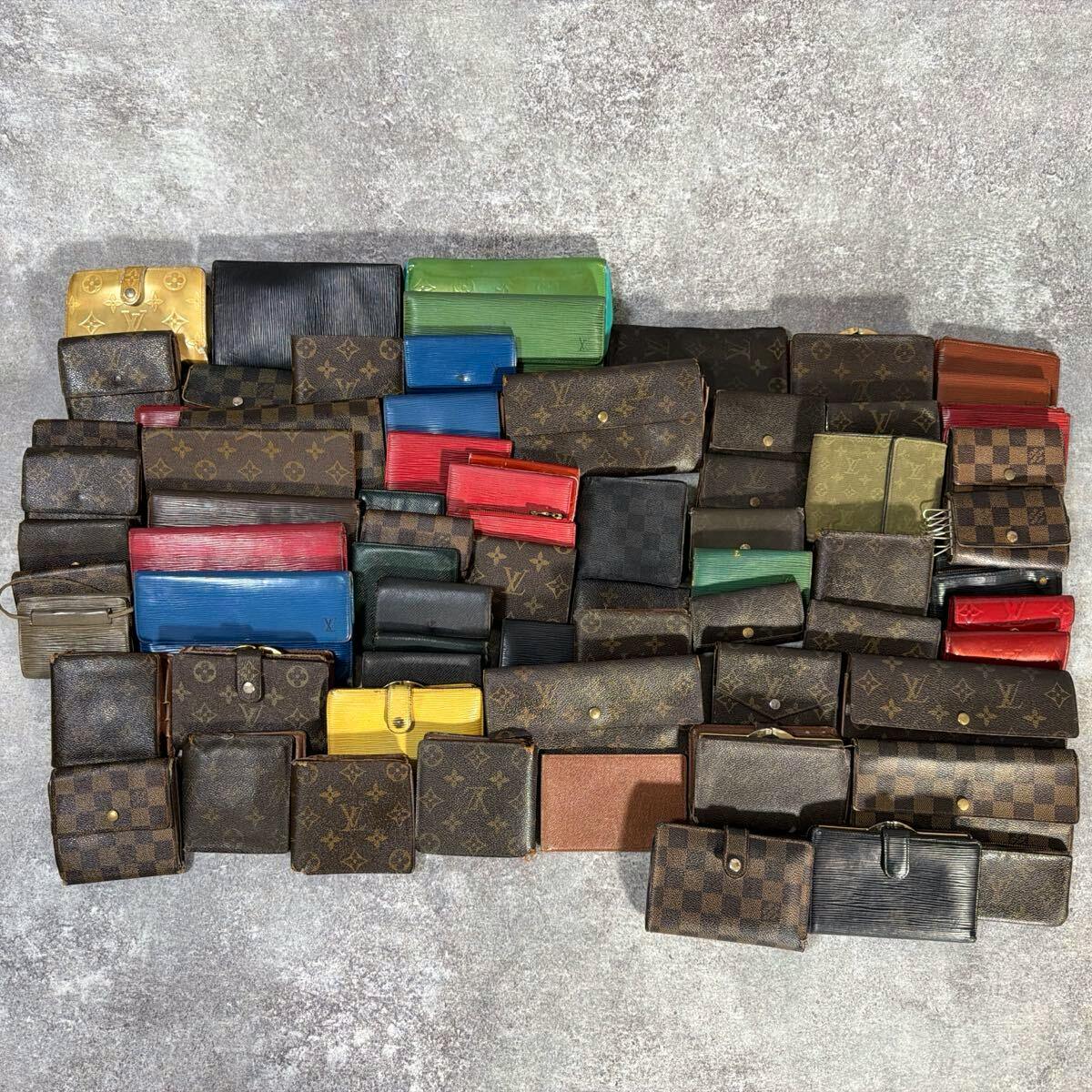 A large assortment of Louis Vuitton wallets and small leather goods in monogram, Damier, and Epi patterns laid out on a textured surface.