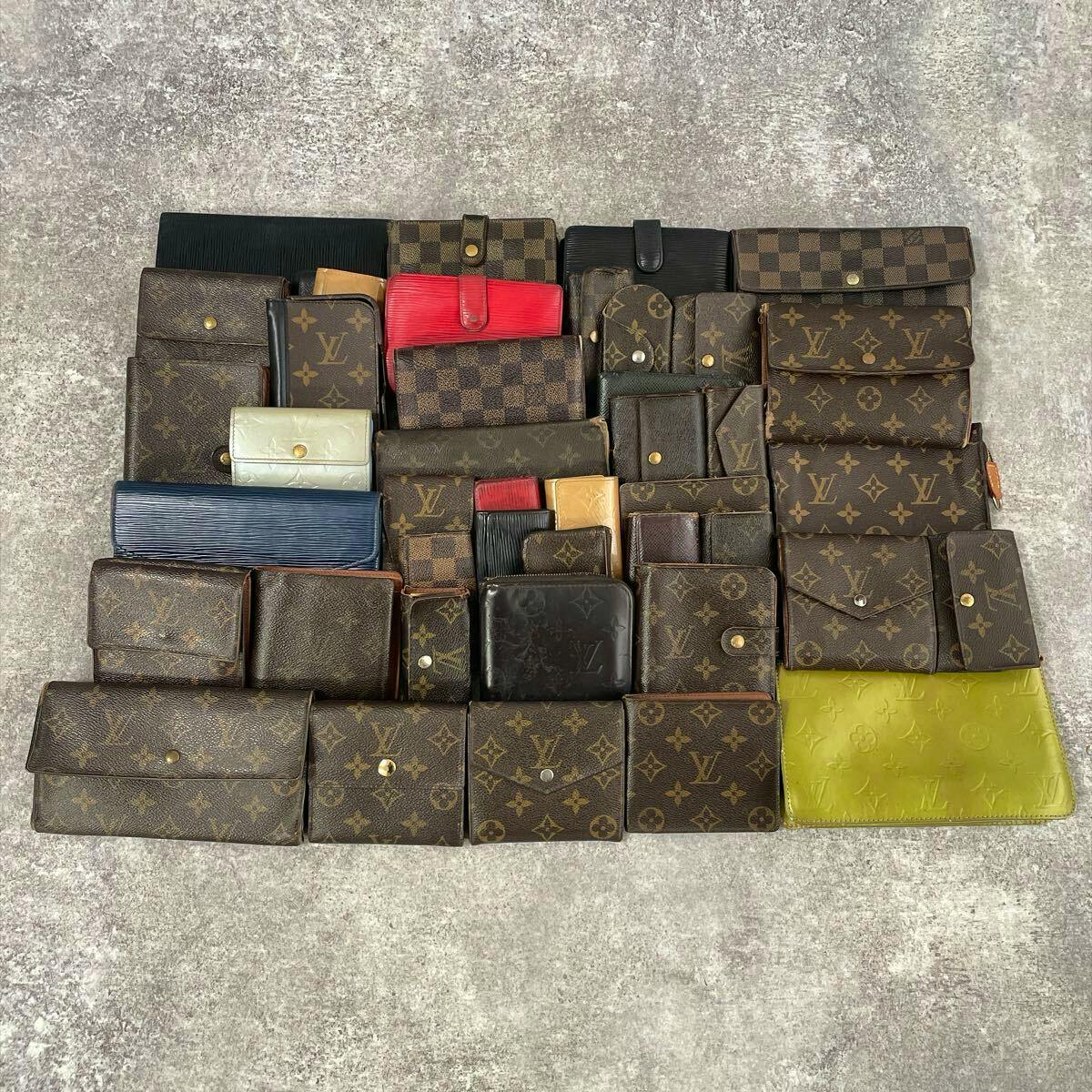 Many Louis Vuitton wallets and small leather goods arranged flat on a gray surface.