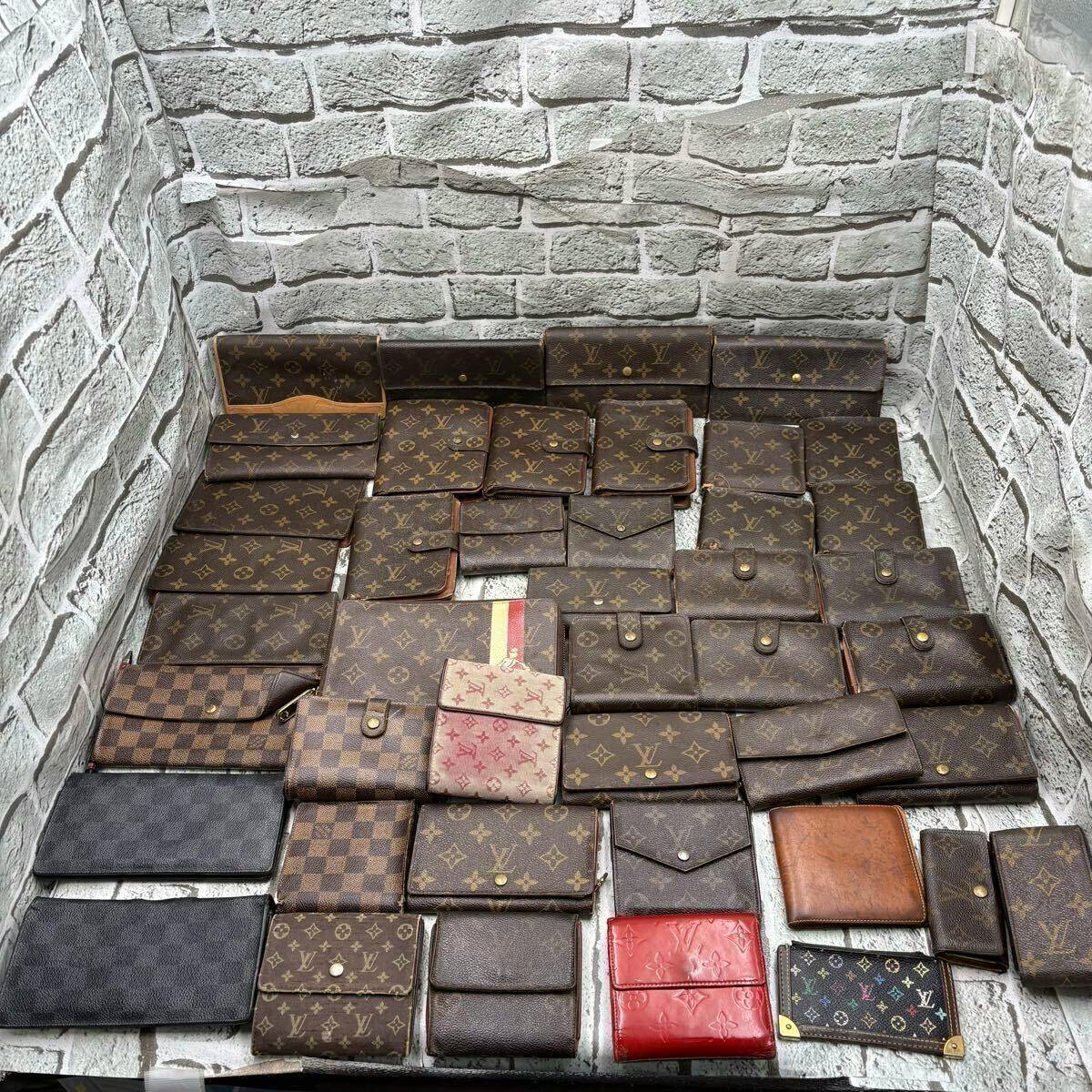 Multiple Louis Vuitton wallets in monogram and Damier patterns arranged on a surface in a corner.