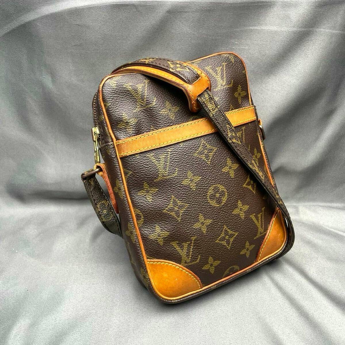 Front view of a Louis Vuitton monogram Danube shoulder bag with leather trim and an adjustable shoulder strap on a gray background.