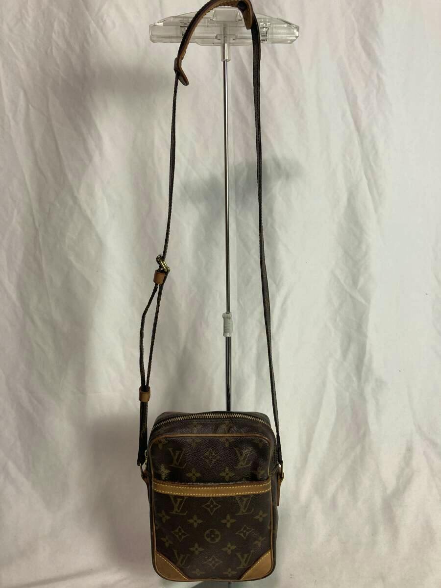 Front view of the Louis Vuitton monogram Danube shoulder bag hanging from a display stand, showing the monogram canvas, front pocket, leather trim, and adjustable strap.