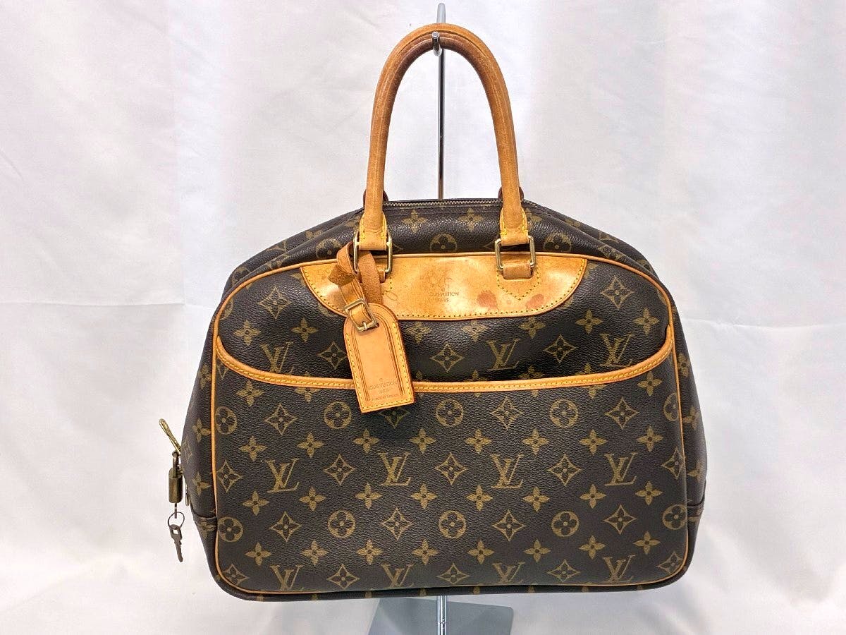 Front view of a Louis Vuitton monogram canvas handbag with two rolled leather top handles, a luggage tag, and a padlock on the side.