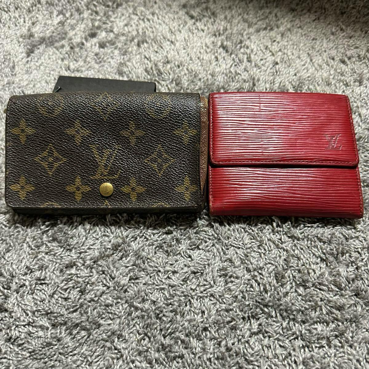 Two Louis Vuitton wallets side by side on a carpet: a monogram canvas wallet and a red Épi leather wallet.
