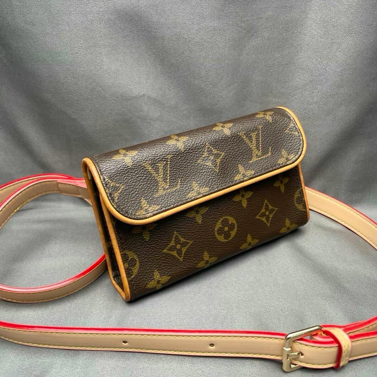 Front view of a Louis Vuitton monogram mini shoulder/crossbody bag with beige leather trim and a red-edged strap on a gray background.