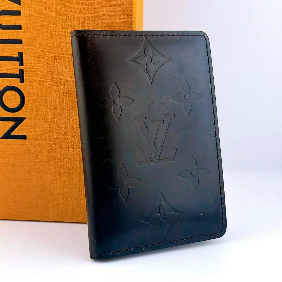 Black monogram-embossed card case standing upright next to an orange Louis Vuitton box.