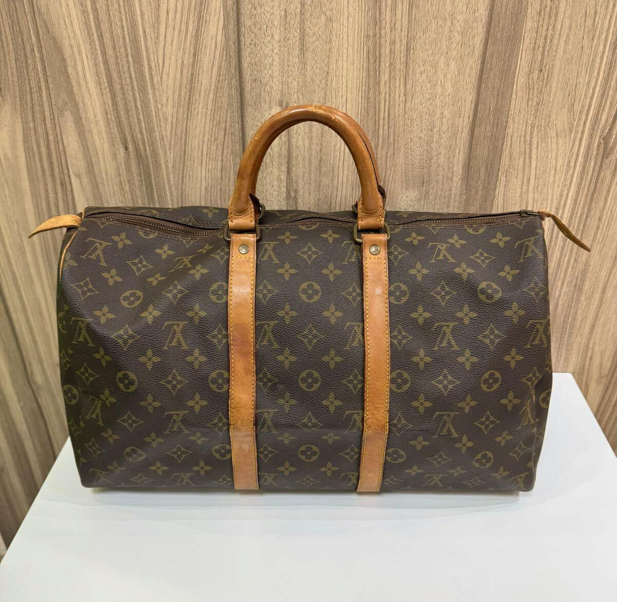 Front view of a Louis Vuitton monogram canvas Keepol 45 duffle bag with leather handles and straps on a white surface against a wooden background.
