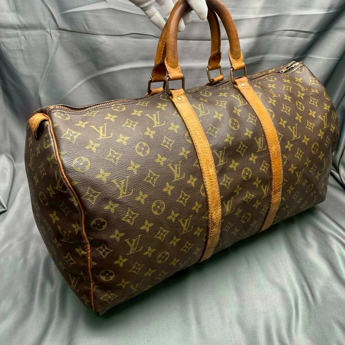 Louis Vuitton monogram canvas duffel bag with patinated leather handles and straps shown on a gray fabric background.