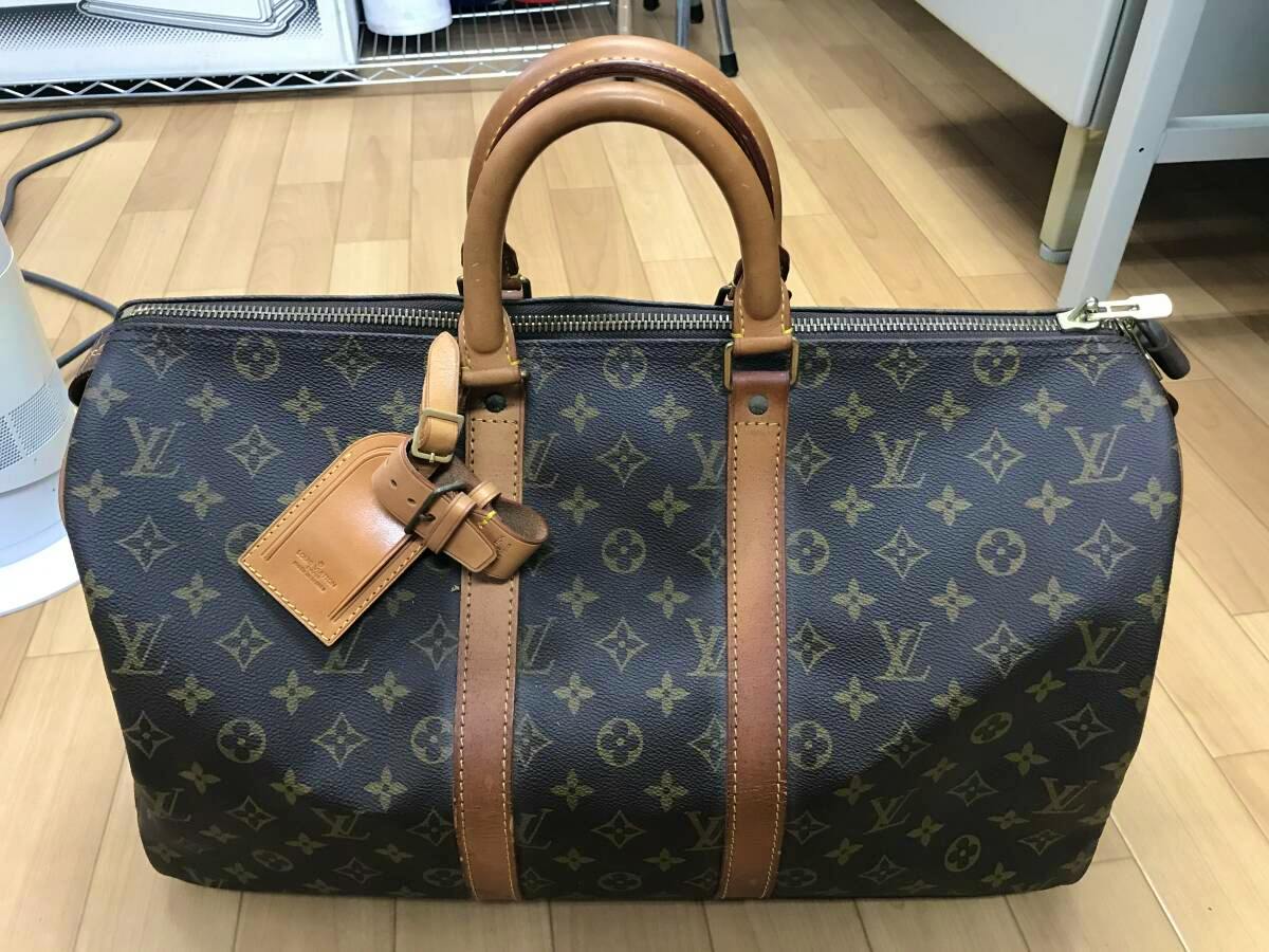 Front view of the LOUIS VUITTON monogram canvas boston bag (45cm) showing leather handles, straps and a luggage tag on a wooden floor.