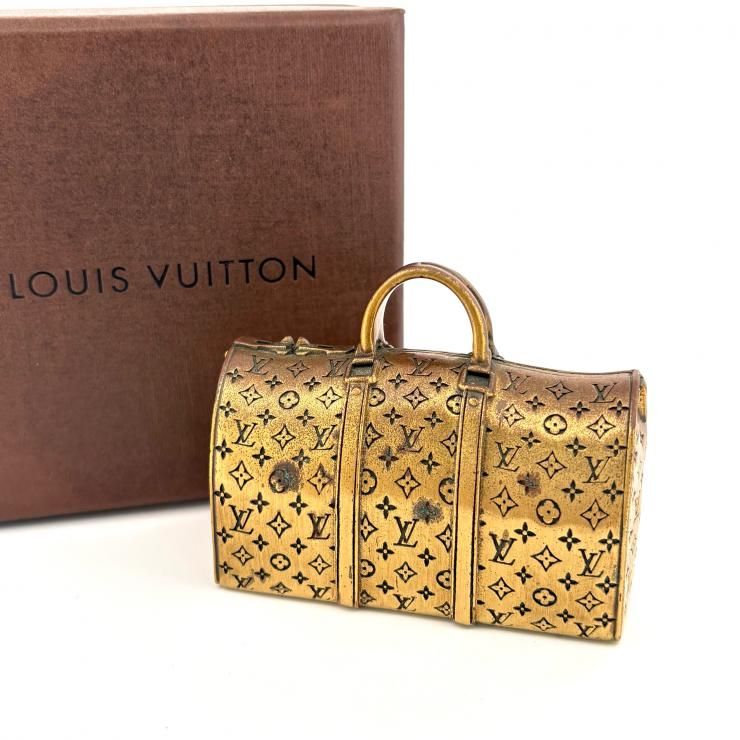 Brass paperweight shaped like a Louis Vuitton monogram Boston bag displayed next to a Louis Vuitton box.
