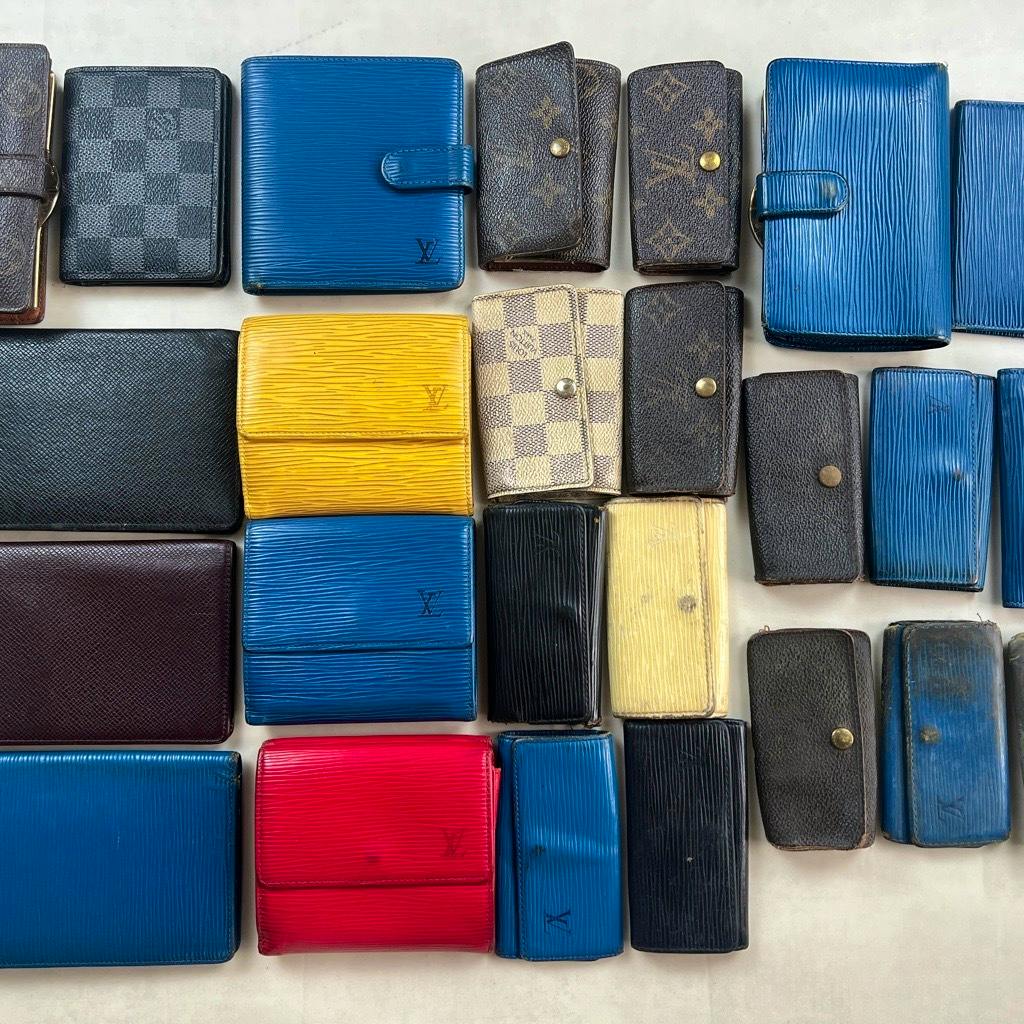 Multiple Louis Vuitton wallets and key holders laid out flat in a grid showing various colors and patterns.
