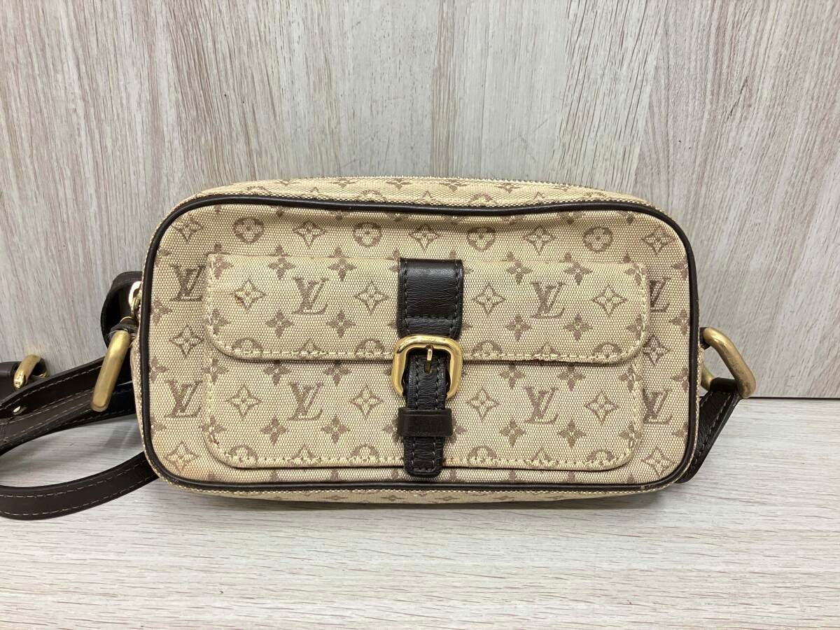 Front view of a beige Louis Vuitton Monogram Mini Juliette shoulder bag with dark brown trim, a front buckle, and an adjustable strap on a light wood surface.