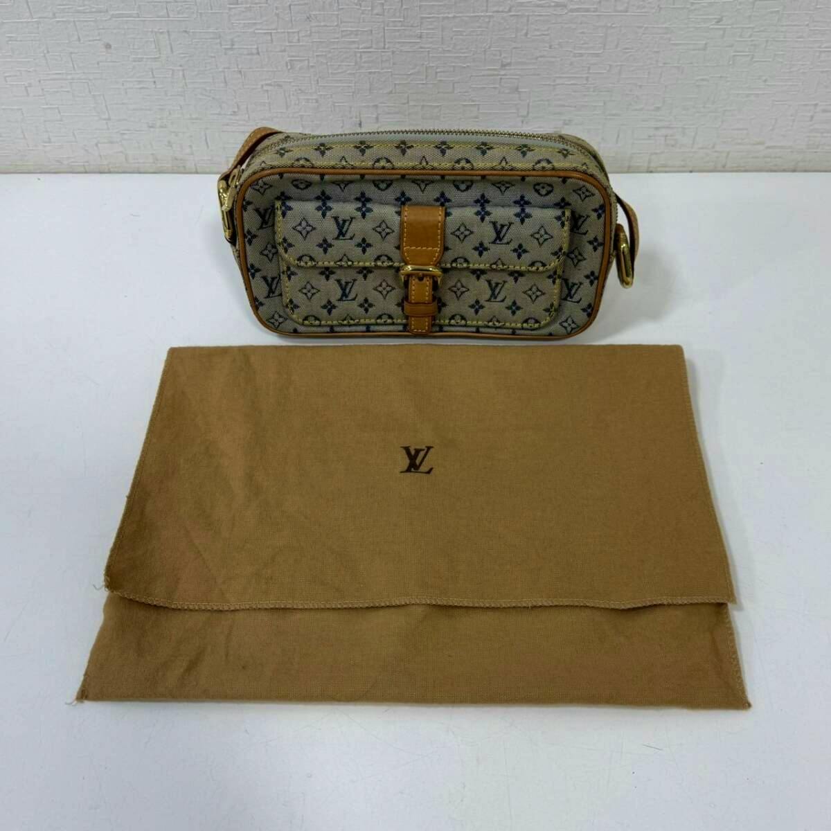 Front view of the Louis Vuitton monogram mini shoulder bag placed behind a brown LV dust bag on a white surface.