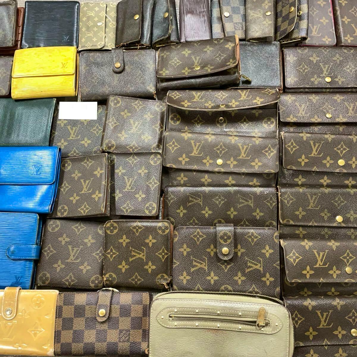 Multiple Louis Vuitton wallets and small leather goods laid out in rows showing monogram and other patterns.