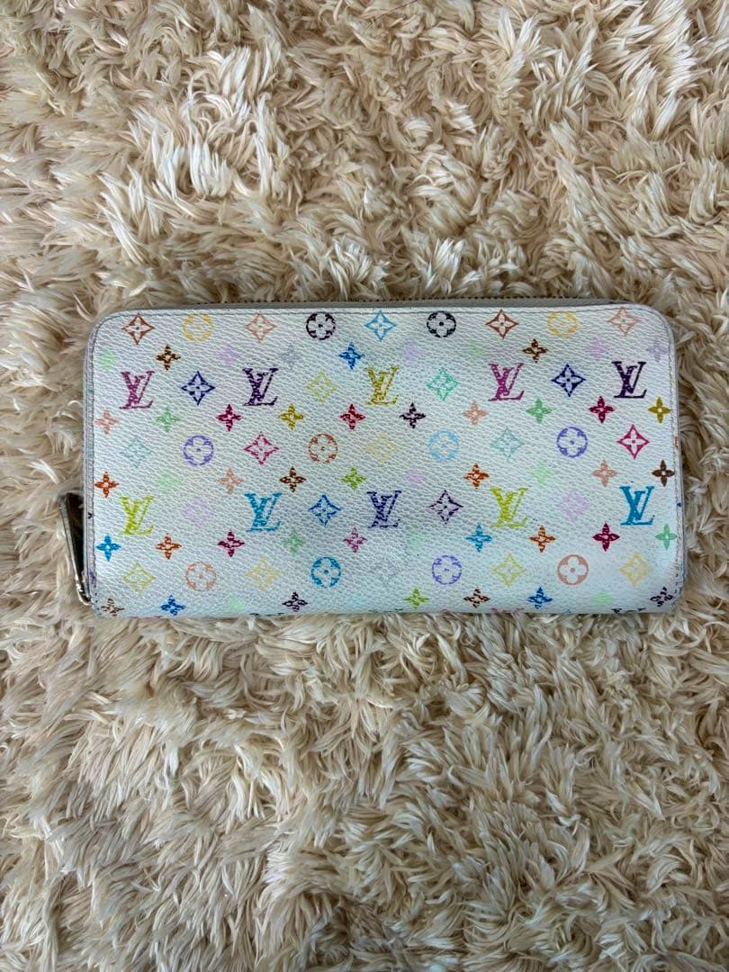 White Louis Vuitton multicolor monogram long wallet laid flat on a beige shag rug, front exterior visible.