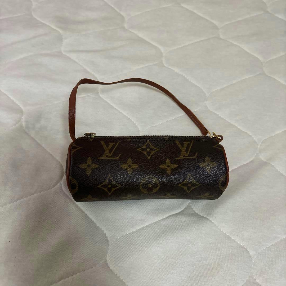 Louis Vuitton monogram Papillon pouch with a leather strap placed on a quilted white surface.