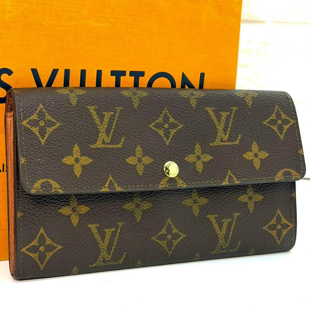 Brown Louis Vuitton monogram wallet with a front flap and gold snap button shown against an orange box.