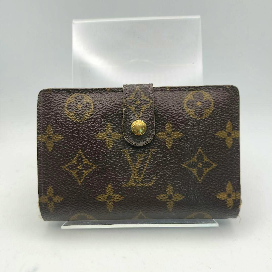 Front of the Louis Vuitton monogram folding wallet with a snap-button tab closure on a clear display stand.
