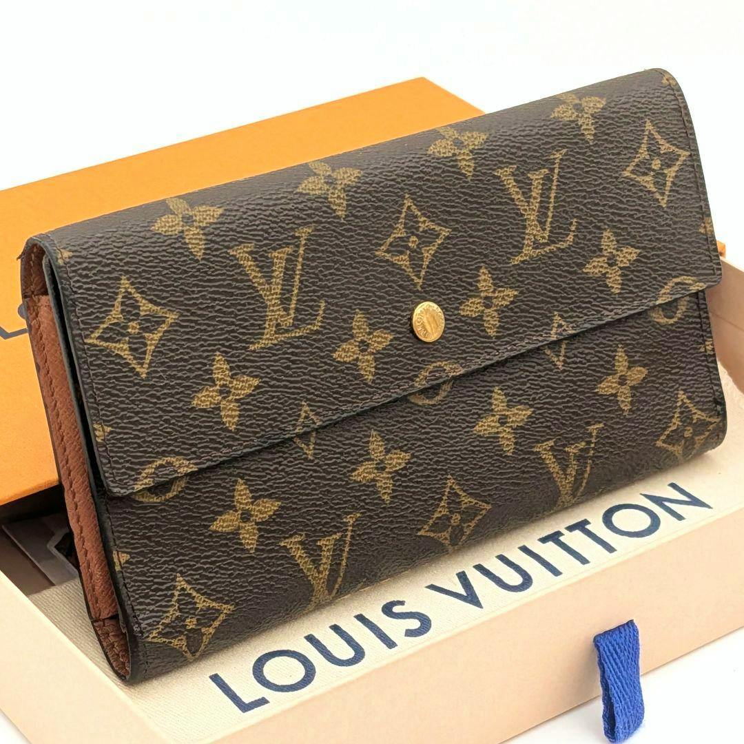 Front view of the Louis Vuitton monogram tri-fold wallet (wallet, cow leather) on a Louis Vuitton box showing the flap with a gold snap button.