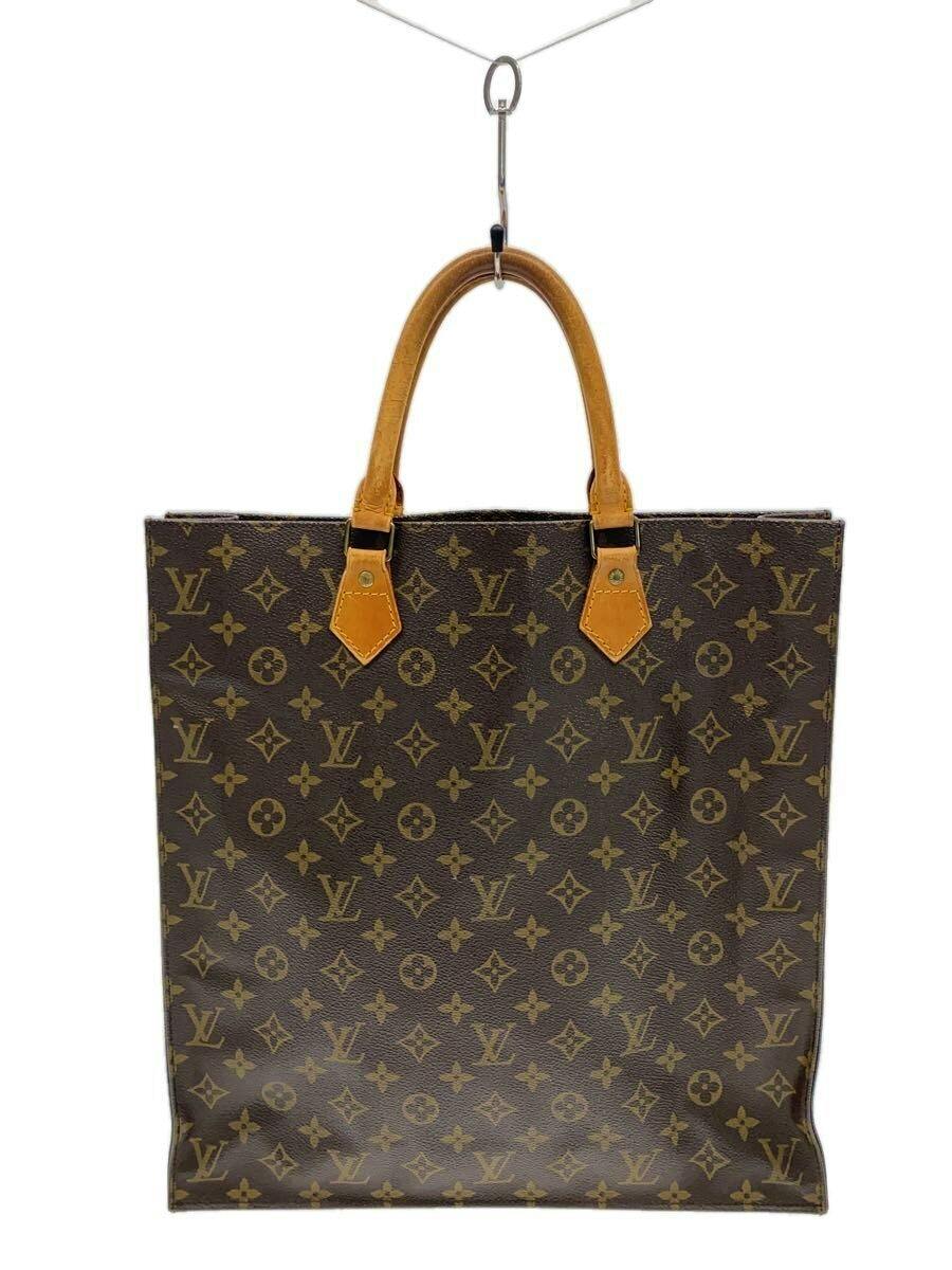 Front view of a brown Louis Vuitton monogram tote bag with tan leather handles hanging from a hook.