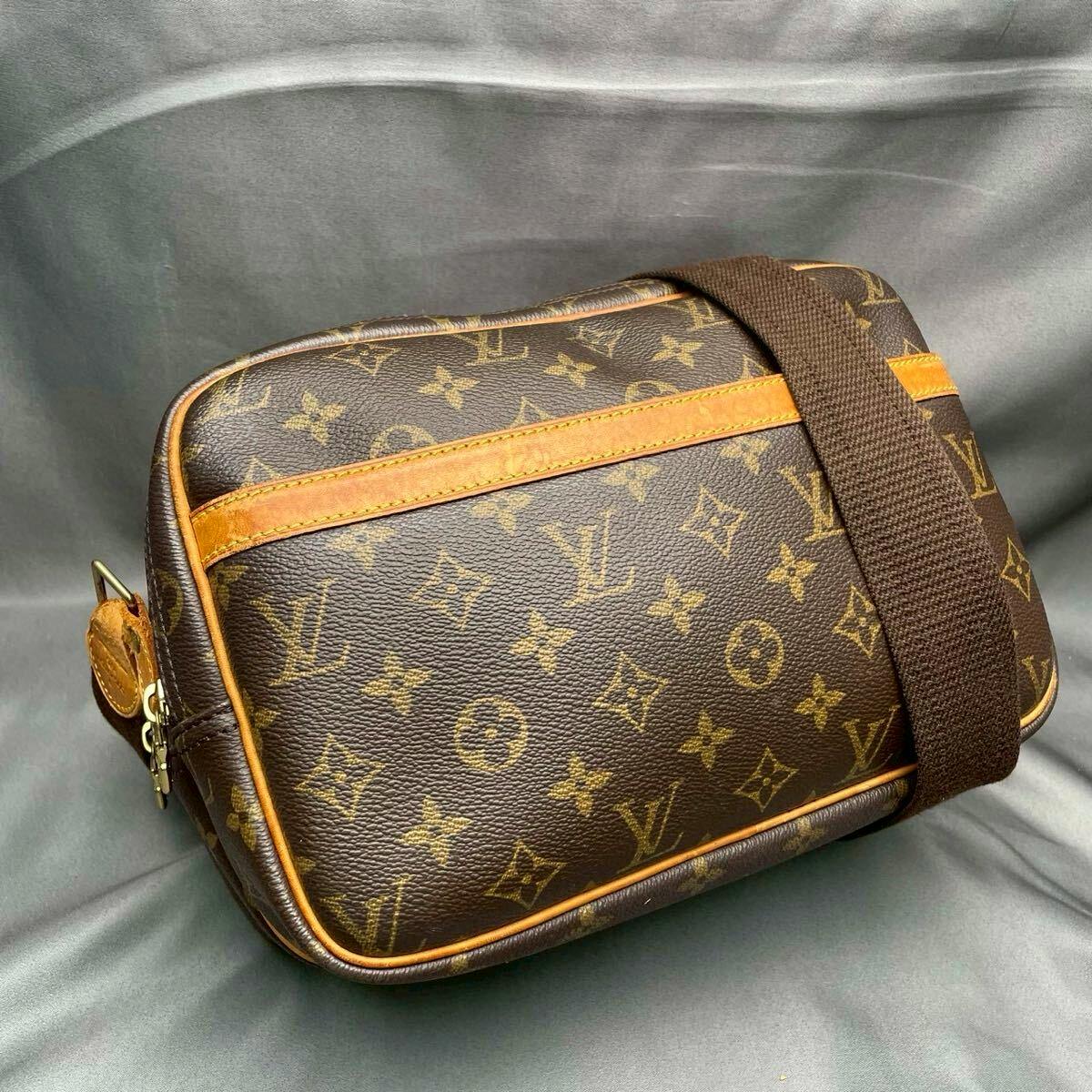Louis Vuitton Monogram Reporter PM crossbody shoulder bag in monogram canvas with leather trim and brown fabric strap on a gray background.