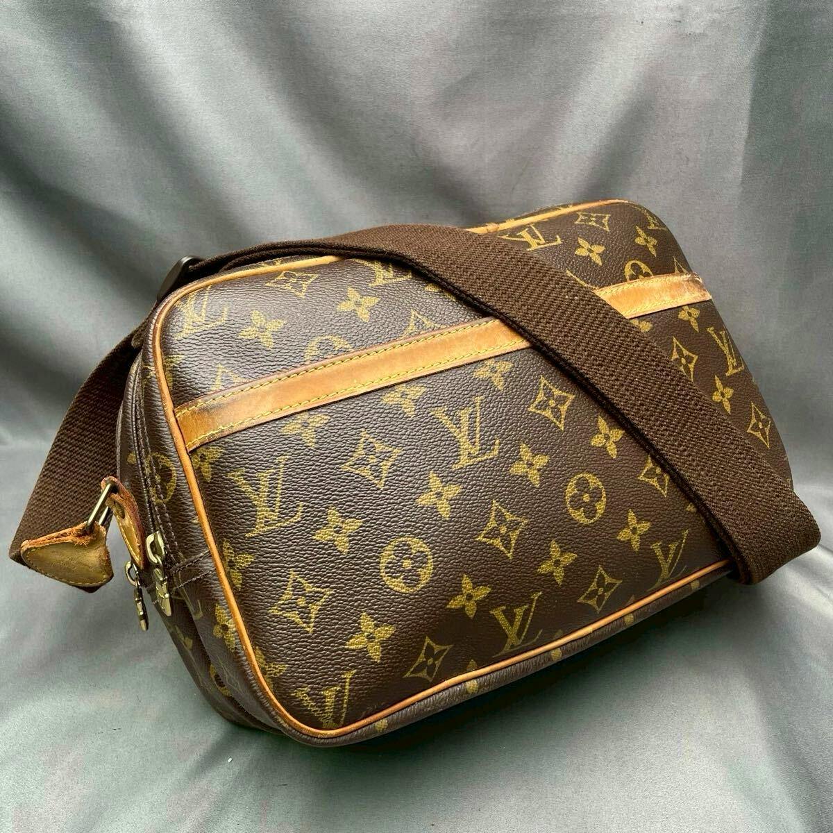 Louis Vuitton Monogram Reporter PM crossbody shoulder bag on a grey background showing monogram canvas, leather trim, and a brown fabric strap.