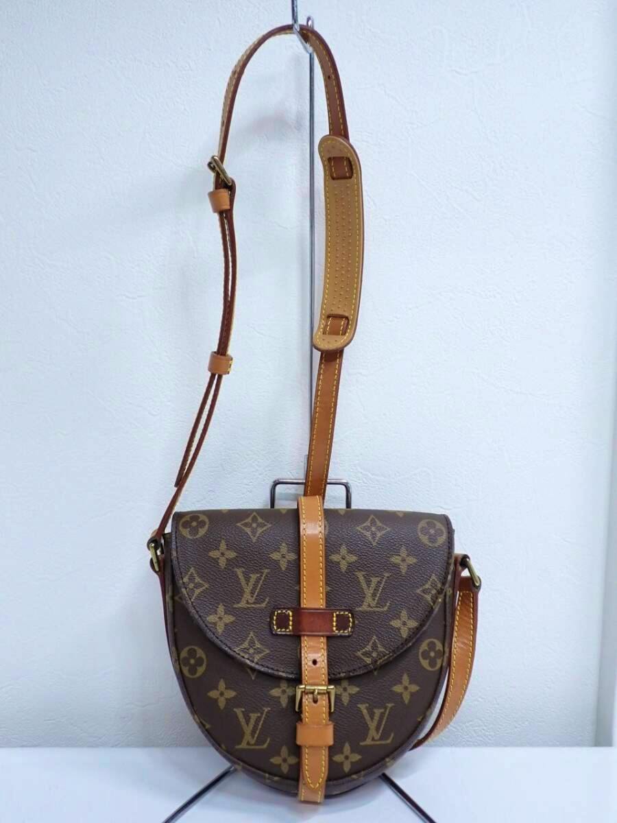 Louis Vuitton monogram canvas shoulder bag with leather strap hanging on a stand against a white background.