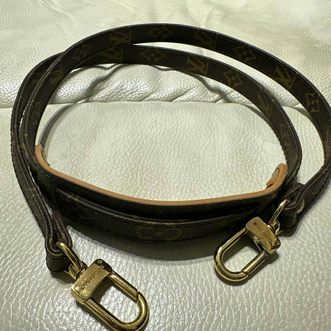Louis Vuitton monogram shoulder strap with a padded shoulder piece and gold-tone clasps laid on a light surface.