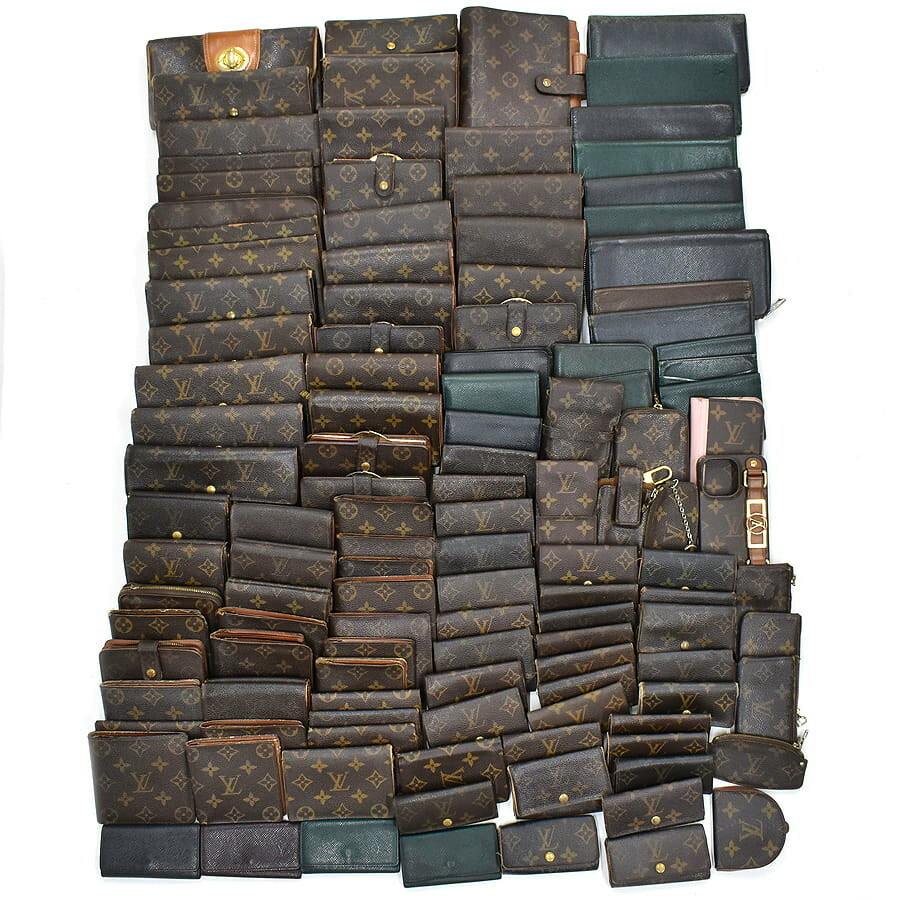 Top-down photo of a large assortment of Louis Vuitton wallets and small leather goods in monogram and dark leathers arranged on a white background.