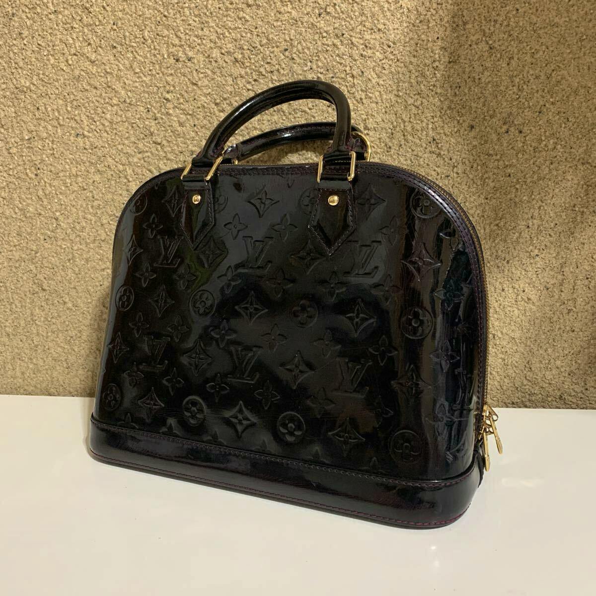 Front view of a purple Louis Vuitton Monogram Vernis Alma handbag showing embossed monogram and top handles on a surface.