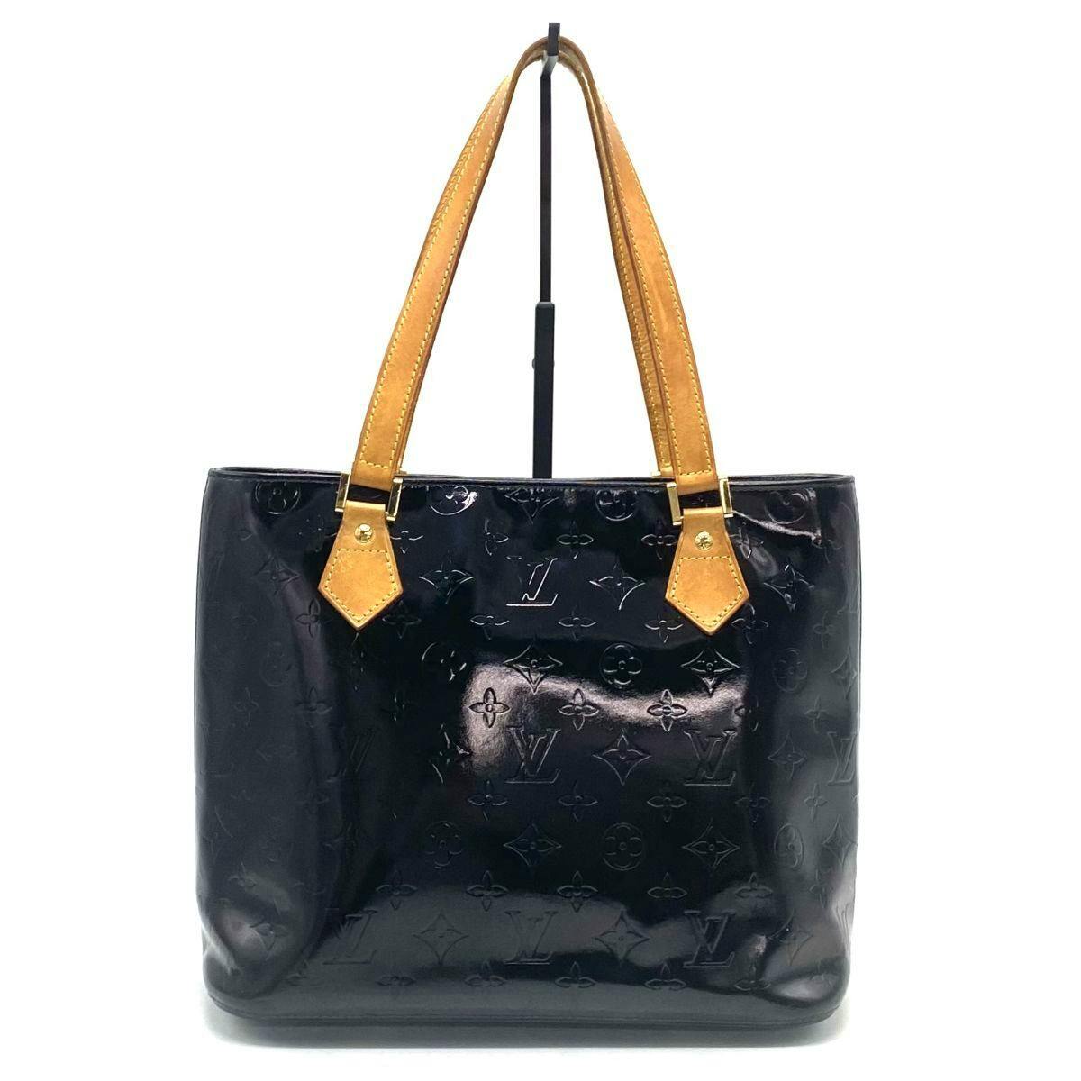 Front view of the Louis Vuitton Monogram Vernis handbag with tan leather handles on a display stand.