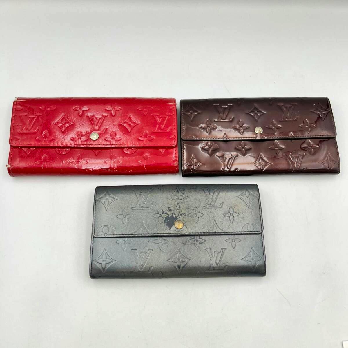 Three Louis Vuitton long wallets (Monogram Vernis) in red, brown, and dark gray arranged on a white background.