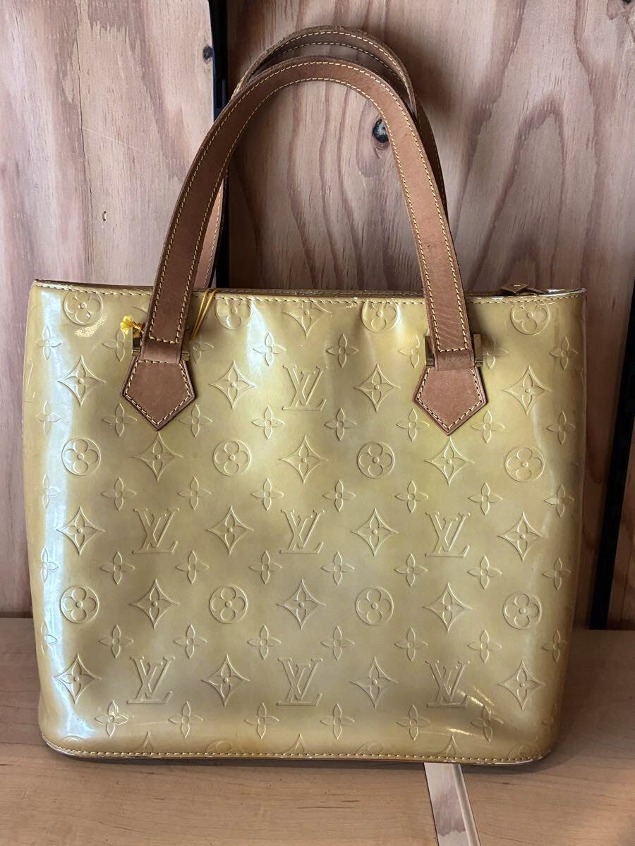 Front view of a yellow Louis Vuitton Monogram Vernis Montebello PM handbag with two leather top handles against a wooden background.