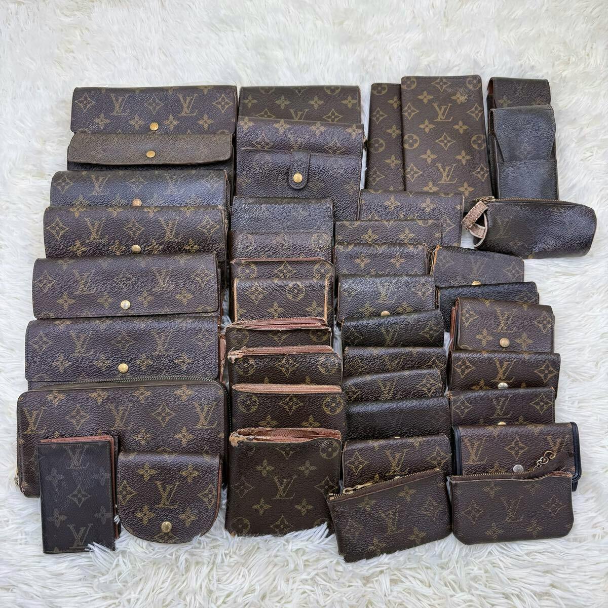 Multiple used Louis Vuitton monogram canvas wallets, pouches, and key cases arranged on a white fur background.