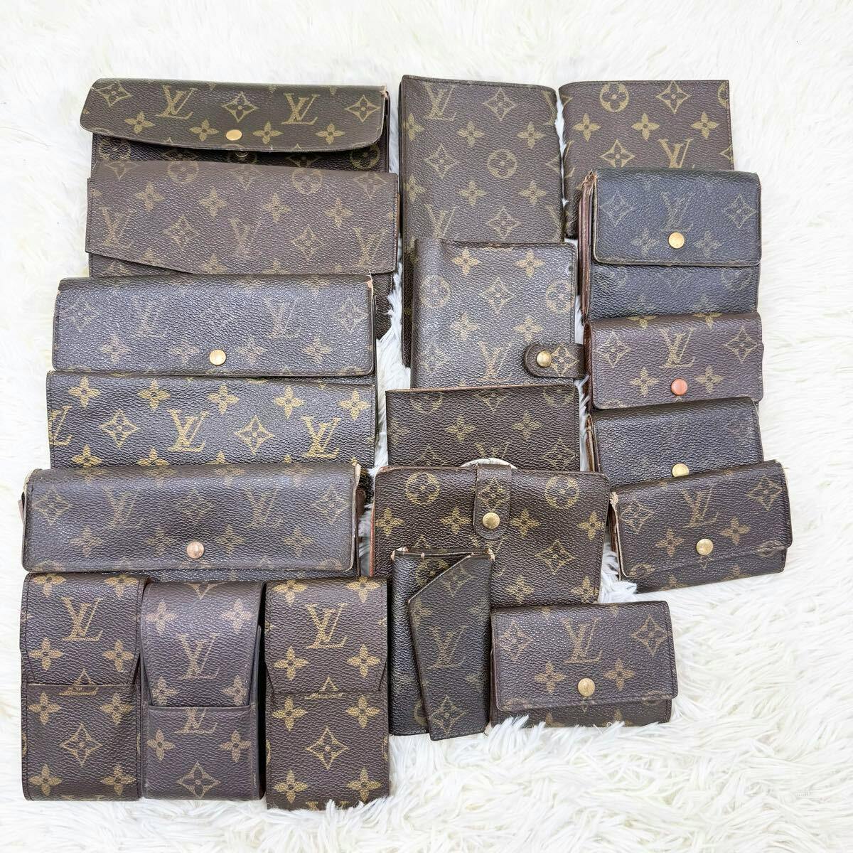 Multiple Louis Vuitton monogram wallets and small cases arranged on a white rug.