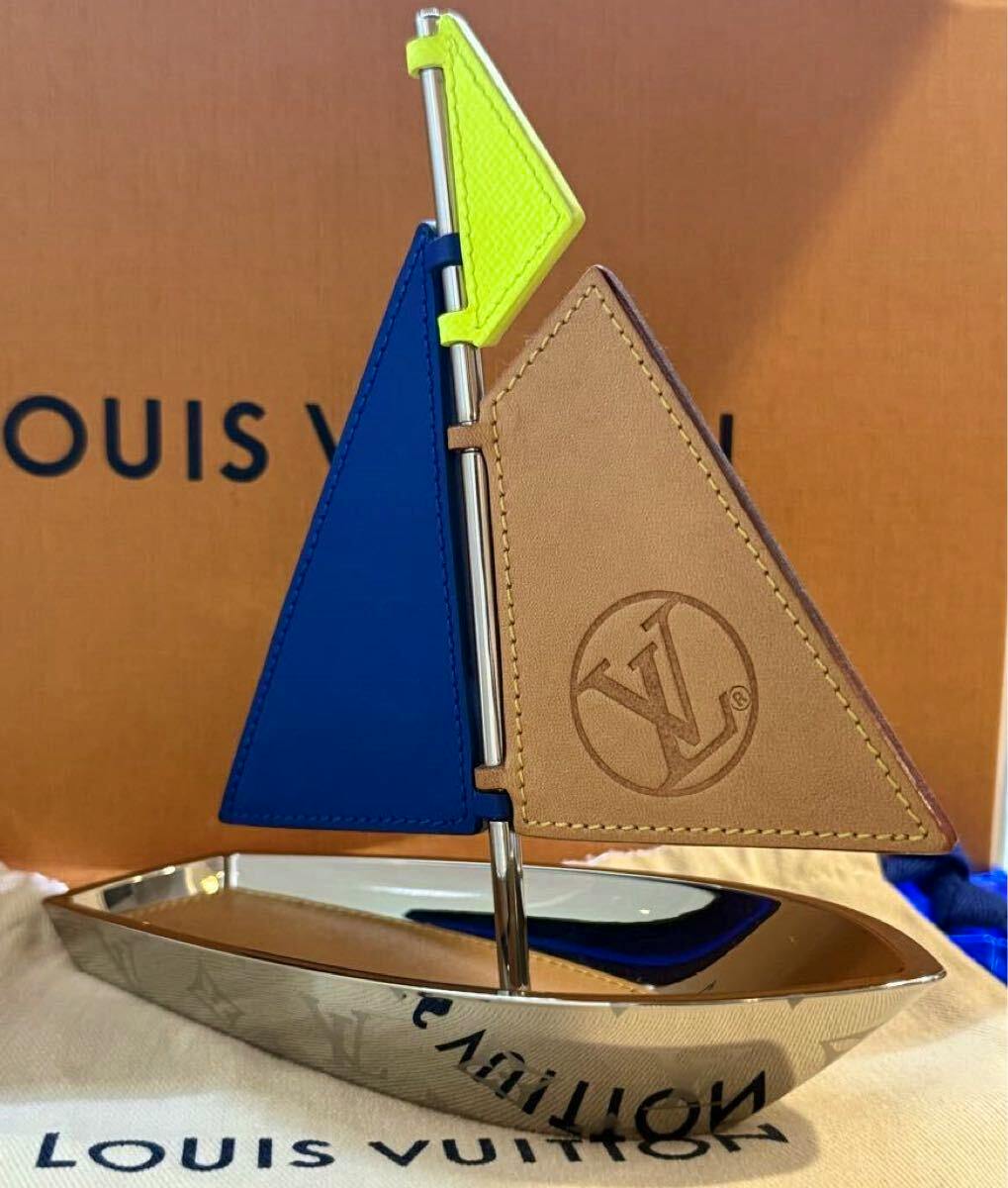 Ornamental metal Louis Vuitton sailboat paperweight with blue and tan leather sails and LV logo.
