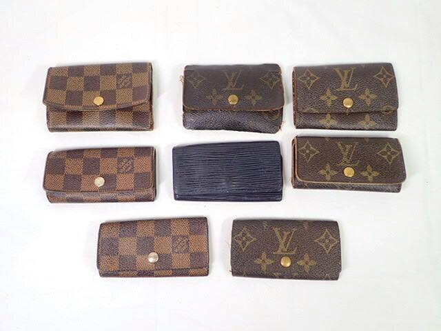 Eight Louis Vuitton key cases in monogram, Damier, and Epi patterns arranged on a white background.