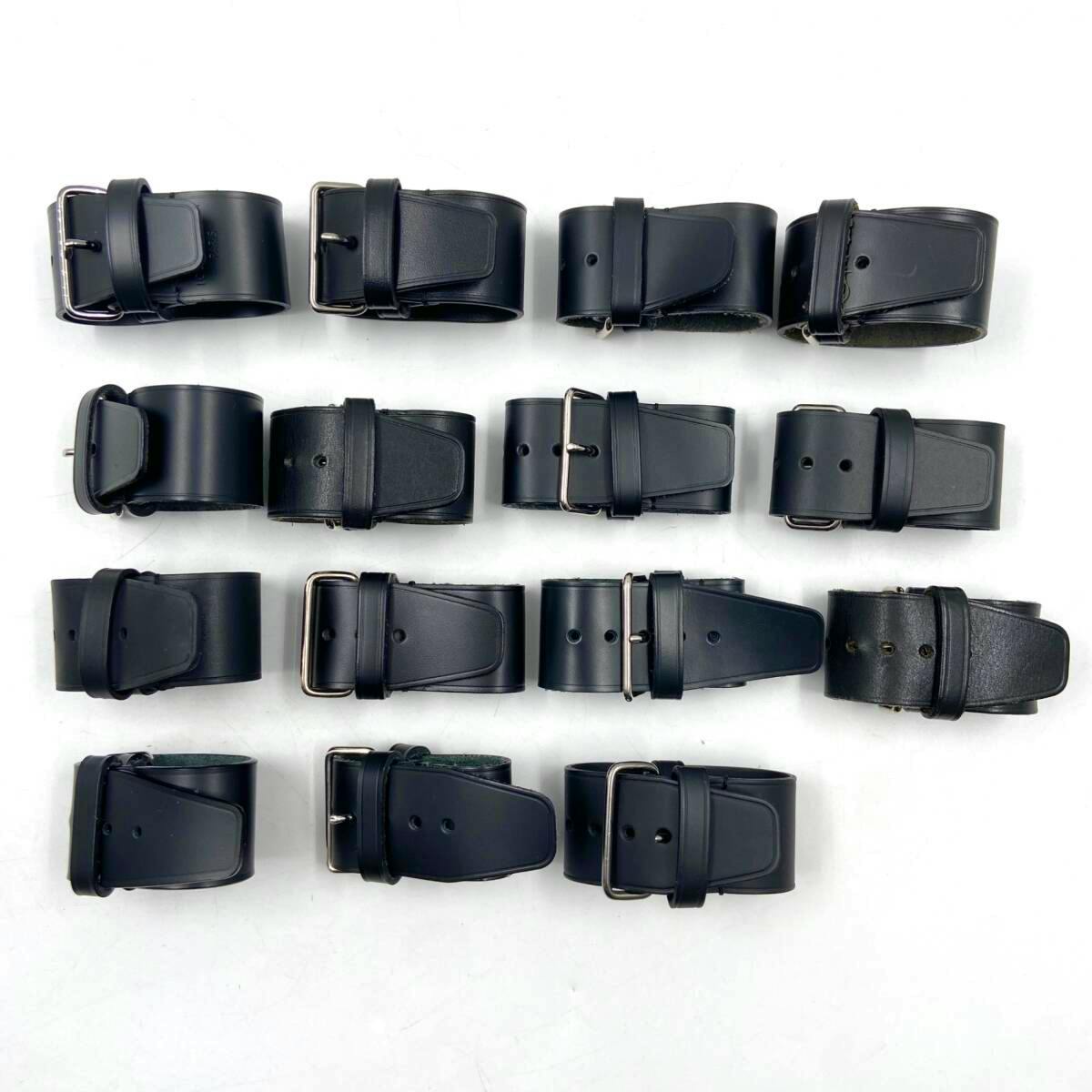 Fifteen black leather Louis Vuitton name-tag belt pieces rolled and arranged in rows on a white background.
