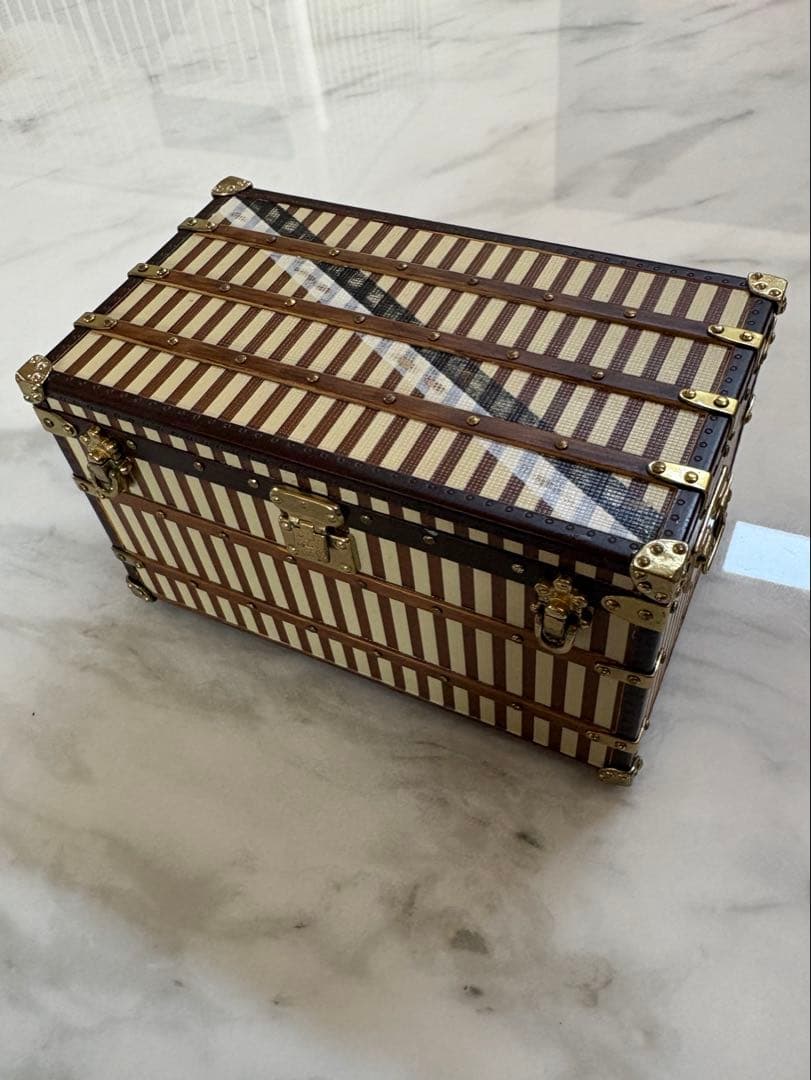 A Louis Vuitton novelty trunk paperweight with striped exterior and brass hardware sitting on a marble surface.