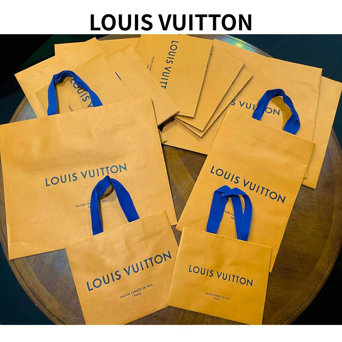 Several orange Louis Vuitton paper shopping bags with blue handles arranged on a wooden table.