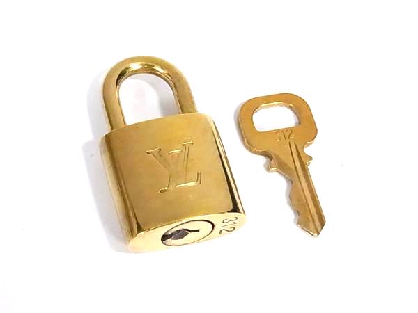 A gold-colored Louis Vuitton padlock with an accompanying key on a white background.