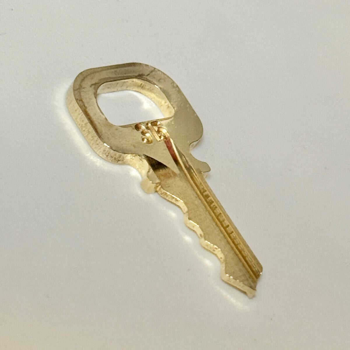 Gold-colored key for a Louis Vuitton padlock stamped "315" on a white background.
